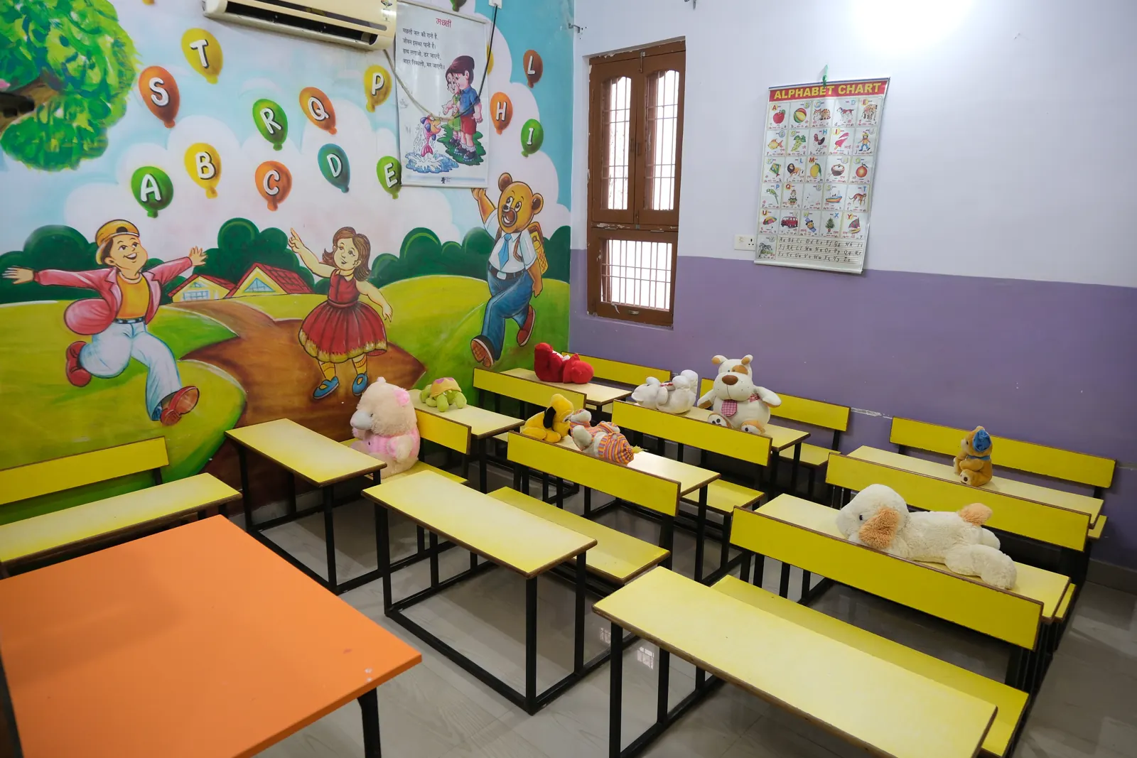 A classroom with yellow desks, soft toys and an alphabet balloon mural