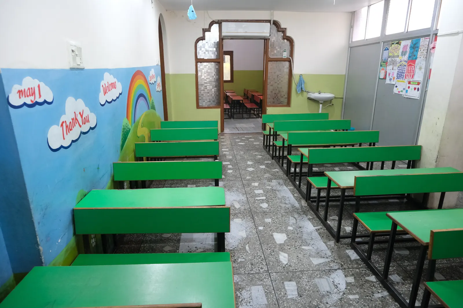 A bright classroom with green desks and rainbow wall art